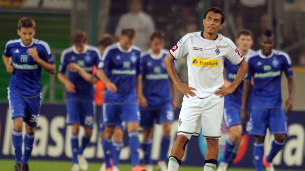 Ein Fußballspieler in weißem Trikot mit „Postbank“-Aufdruck steht auf dem Spielfeld.