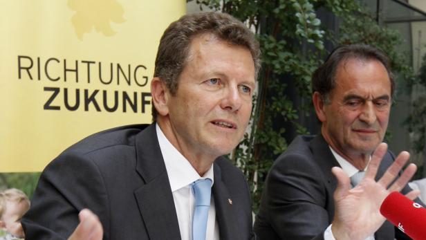 Zwei Männer in Anzügen sitzen vor einem Banner mit der Aufschrift „Richtung Zukunft“.