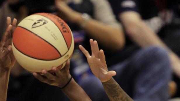 Ein Basketball wird von mehreren Händen gehalten.