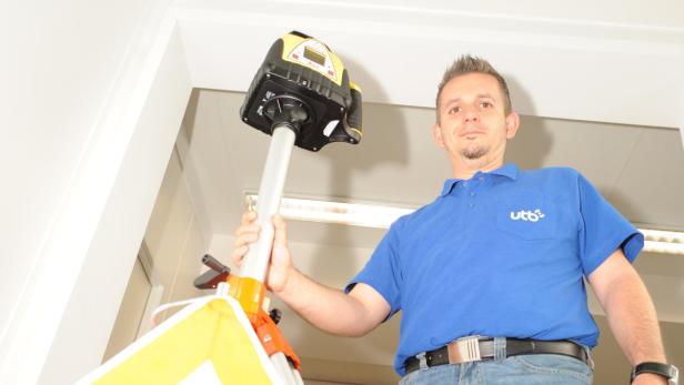 Ein Mann mit blauem Poloshirt bedient ein gelbes Nivelliergerät auf einem Stativ.