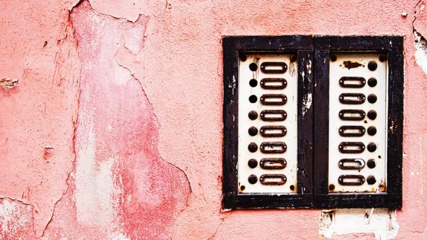 Eine alte Klingelanlage an einer rosafarbenen, verwitterten Wand.