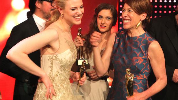Mehrere Frauen mit goldenen Statuen lächeln auf einer Preisverleihung.