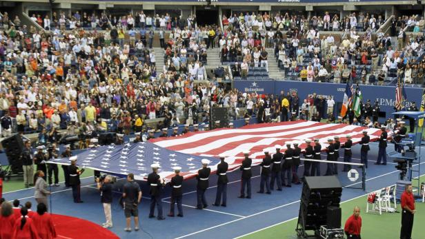 Eine große amerikanische Flagge wird während einer Veranstaltung auf einem Tennisplatz von Soldaten gehalten.