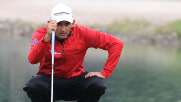 Ein Golfspieler kauert und zielt mit seinem Putter auf dem Grün.