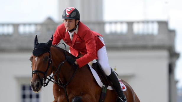 Ein Reiter in roter Jacke auf einem braunen Pferd beim Springreiten.