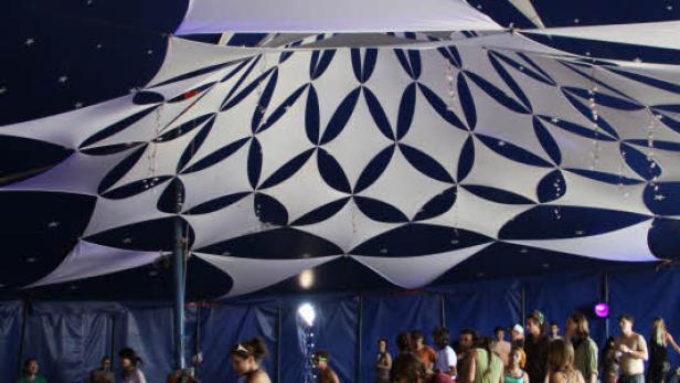 Menschen tanzen unter einem Zirkuszelt mit blauem Sternenhimmel.