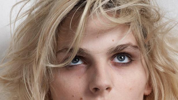 Nahaufnahme des Gesichts einer Frau mit blonden Haaren und blauen Augen, die nach oben blickt.
