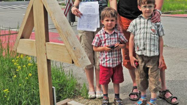 Eine Familie steht an einer Gedenkstätte mit einem Holzkreuz und einer Laterne.