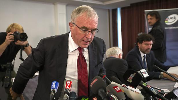 Ein Mann in Anzug spricht vor einer Gruppe von Mikrofonen verschiedener Sender.