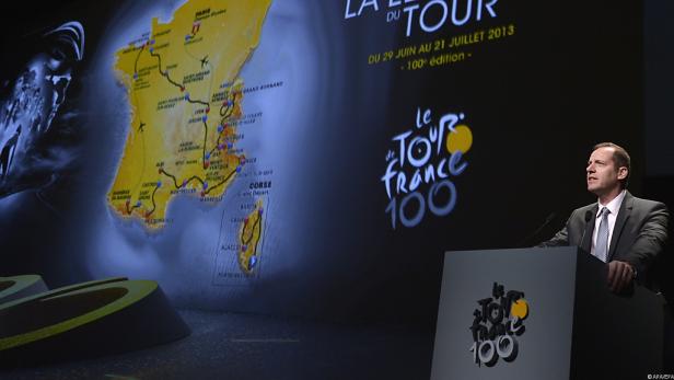 Ein Mann steht an einem Rednerpult vor einer Karte der Tour de France 2013.