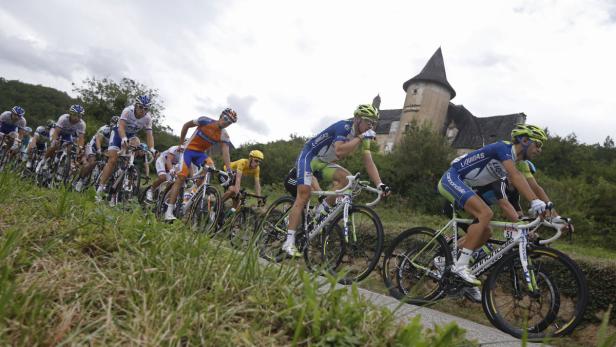 Eine Gruppe Radfahrer fährt ein Rennen auf einer Straße mit einem Schloss im Hintergrund.