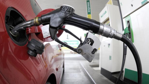 Eine Zapfpistole steckt in einem roten Auto an einer Tankstelle.
