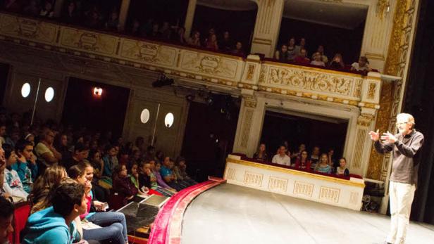 Ein Mann spricht auf einer Bühne vor einem Publikum in einem Theater.
