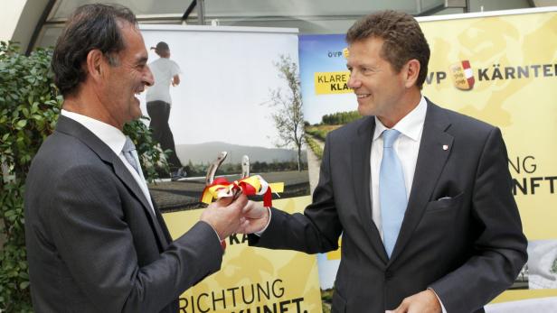 Zwei Männer im Anzug überreichen sich Hufeisen mit einer Schleife in den Kärntner Farben.