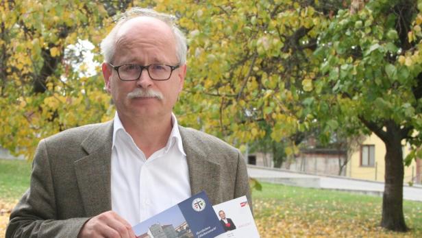 Ein Mann mit Brille und Schnurrbart hält Broschüren in einem Park.