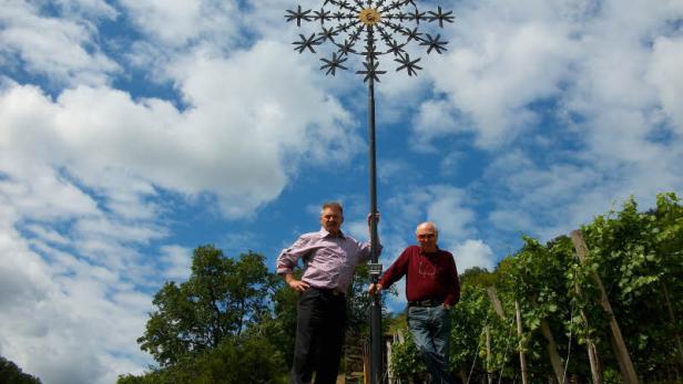 Zwei Männer stehen vor einer großen, sternförmigen Windskulptur unter blauem Himmel.