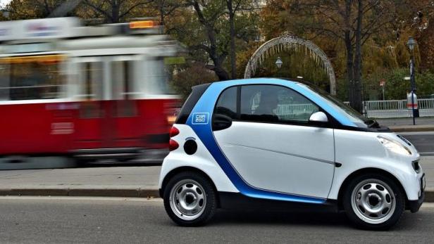 Ein weißer Smart steht am Straßenrand, während eine rote Straßenbahn vorbeifährt.