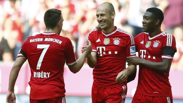 Drei Fußballspieler des FC Bayern München umarmen sich und lachen.