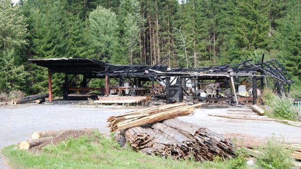 Die Überreste eines abgebrannten Holzschuppens vor einem Wald.