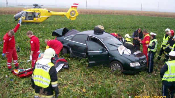 Ein Auto ist in einem Feld verunglückt, Rettungskräfte und ein Hubschrauber sind vor Ort.