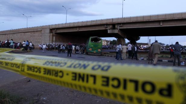Ein beschädigter Bus steht unter einer Brücke, umgeben von Menschen und Absperrband der Polizei.