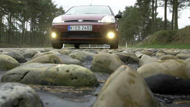 Ein roter Ford Fiesta fährt über eine holprige, steinige Straße.