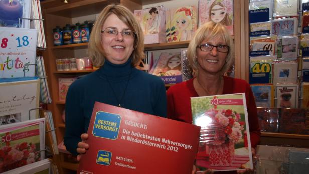 Zwei Frauen präsentieren Auszeichnungen und Glückwunschkarten in einem Geschäft.