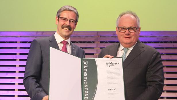 Zwei Männer in Anzügen halten eine Urkunde mit der Aufschrift „Mit Mensch Gruft“.