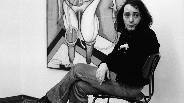 Ein Mann sitzt auf einem Stuhl und raucht vor einem abstrakten Gemälde.