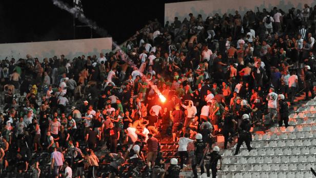 Auf der Tribüne eines Stadions zünden Fans Bengalos und es kommt zu Auseinandersetzungen.