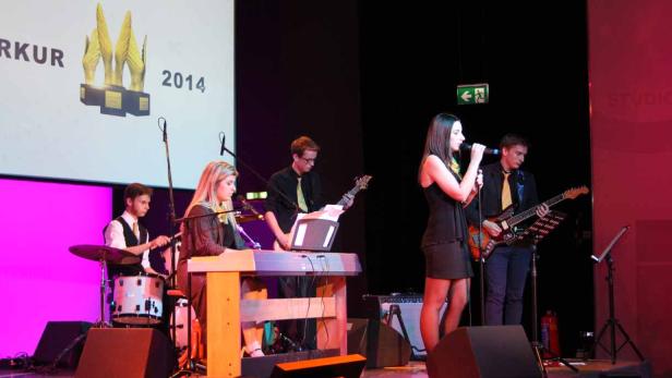 Eine Band tritt auf einer Bühne vor einer Leinwand mit der Aufschrift „2014“ auf.