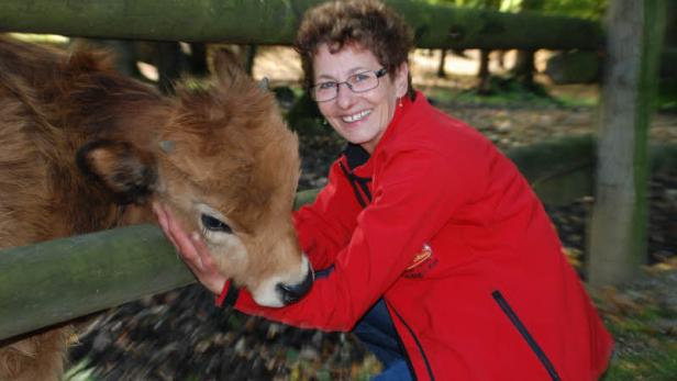 Eine Frau in roter Jacke streichelt ein kleines, braunes Kalb.