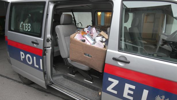 Ein Karton voller beschlagnahmter Gegenstände steht in einem Polizeiwagen.