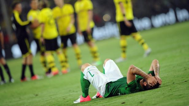 Ein enttäuschter Fußballspieler liegt auf dem Rasen, die Hände vors Gesicht geschlagen.