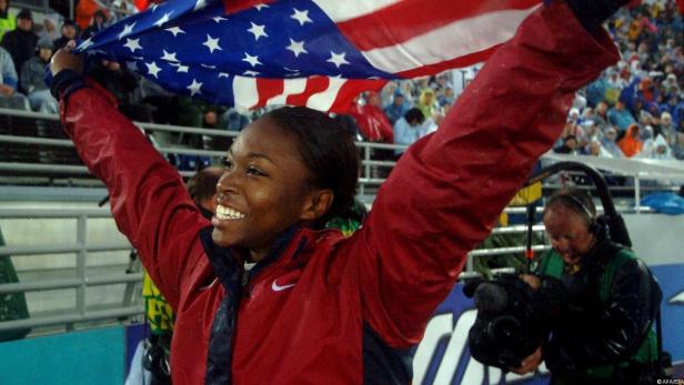 Eine Athletin jubelt mit der US-amerikanischen Flagge in der Hand.
