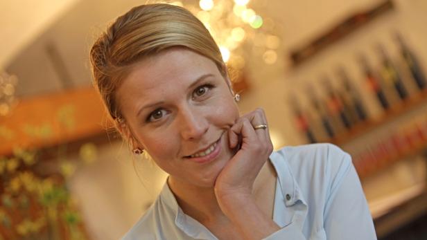 Eine lächelnde Frau mit blonden Haaren stützt ihr Kinn auf ihre Hand.