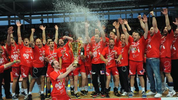 Eine jubelnde Handballmannschaft feiert mit Pokal und Champagner den Meistertitel.