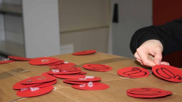 Eine Hand ordnet rote, runde Aufkleber mit einem schwarzen Symbol auf einem Karton an.