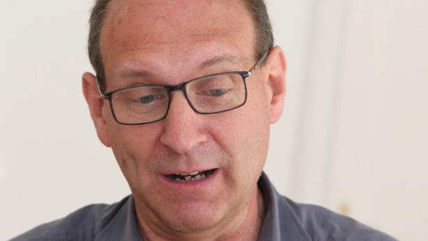 Ein Mann mit Brille und grauem Haar schaut nach unten und spricht.