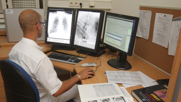 Ein Arzt betrachtet Röntgenaufnahmen und Patientendaten an drei Monitoren.
