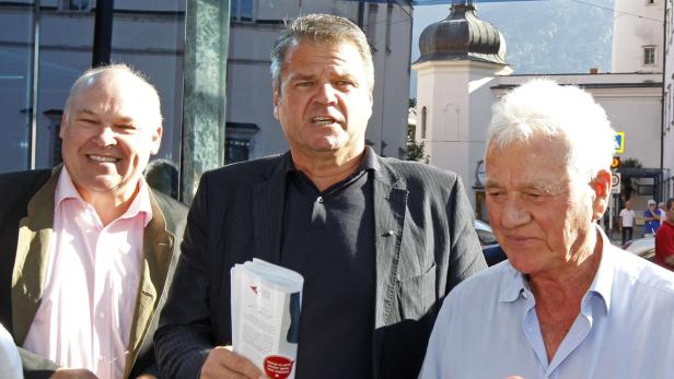 Drei Männer stehen vor einem Gebäude mit einem Turm im Hintergrund.