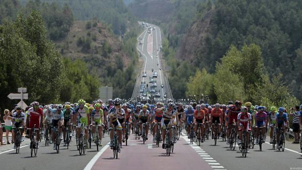Eine große Gruppe Radfahrer fährt auf einer Straße durch eine hügelige Landschaft.
