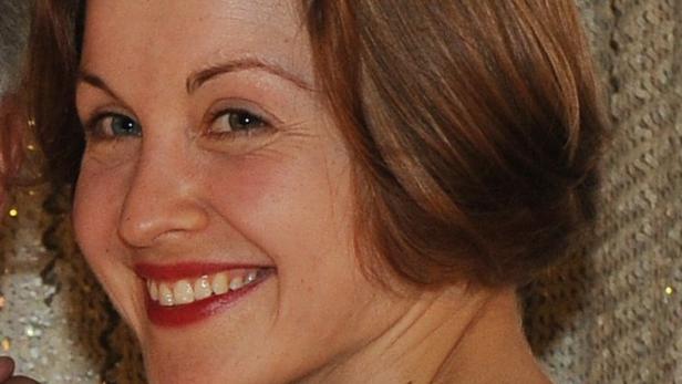 Eine lächelnde Frau mit roten Lippen und braunen Haaren.