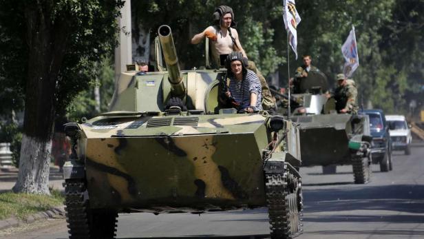 Militärfahrzeuge mit Soldaten fahren auf einer Straße.