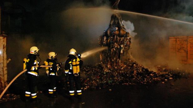 Drei Feuerwehrleute löschen einen brennenden Müllberg mit Wasserwerfern.