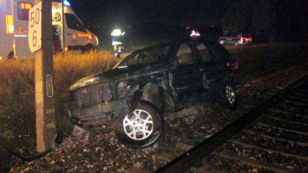 Ein Auto ist bei Nacht auf einem Bahngleis verunglückt; im Hintergrund sind Rettungsfahrzeuge zu sehen.
