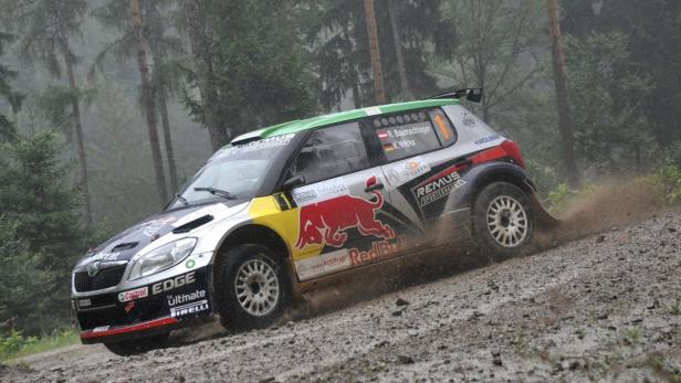 Ein Rallyeauto fährt auf einer schlammigen Strecke durch einen Wald.