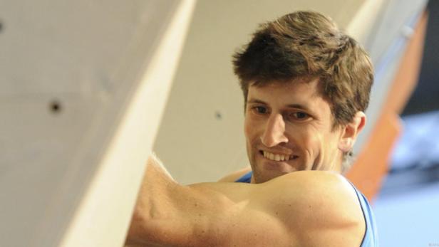 Ein Mann klettert an einer Kletterwand und lächelt.