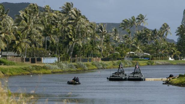 Zwei Militärboote fahren auf einem Fluss, gesäumt von Palmen.