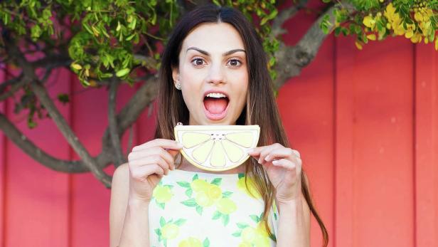 Eine Frau hält eine zitronenförmige Geldbörse vor ihrem zitronenbedruckten Kleid.